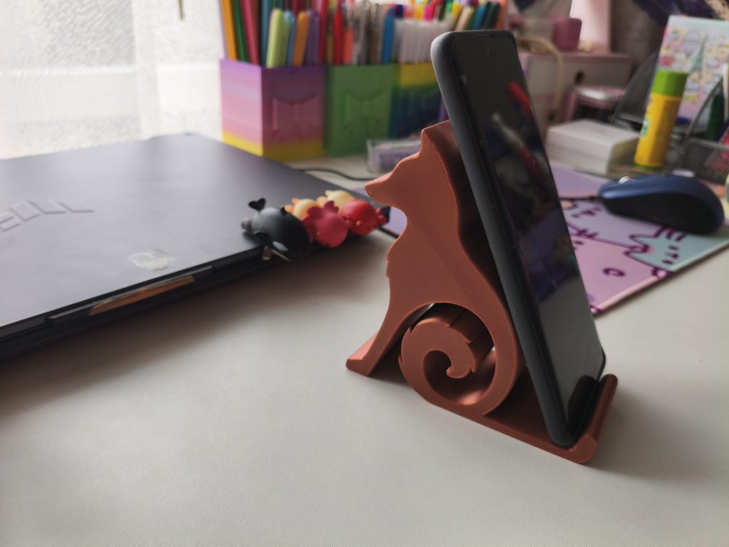 Brązowy stojak na telefon w kształcie zwierzaka na biurku z laptopem