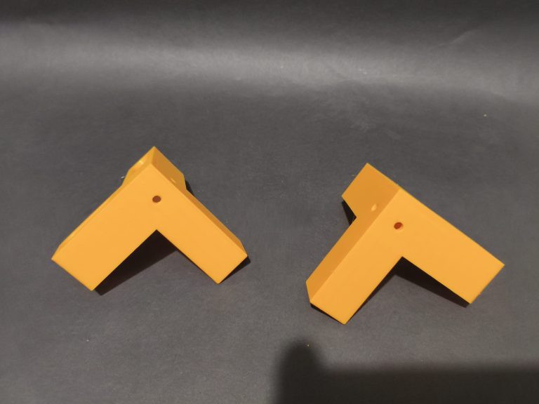 Dwa pomarańczowe kątowniki stolarskie z druku 3D na ciemnym tle